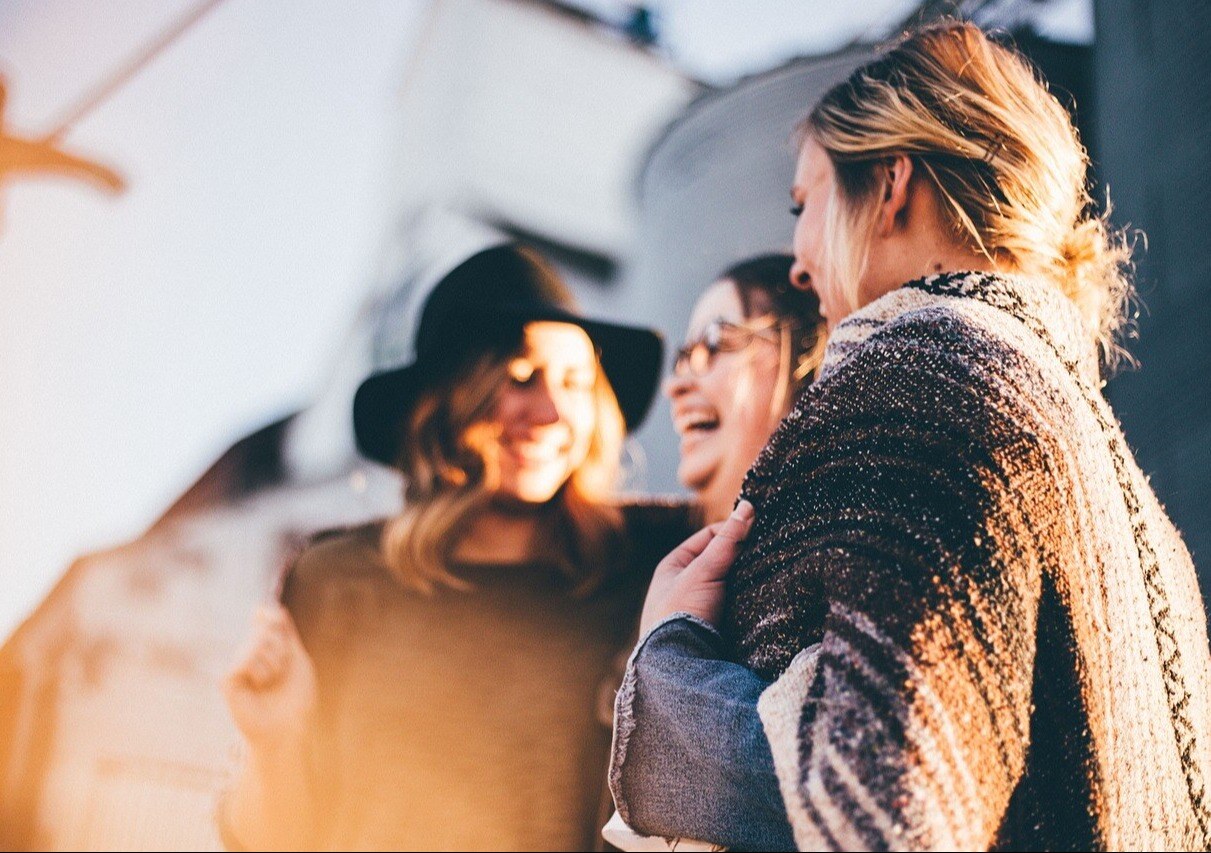 Drie jonge vrouwen staan lachend voor een gebouw